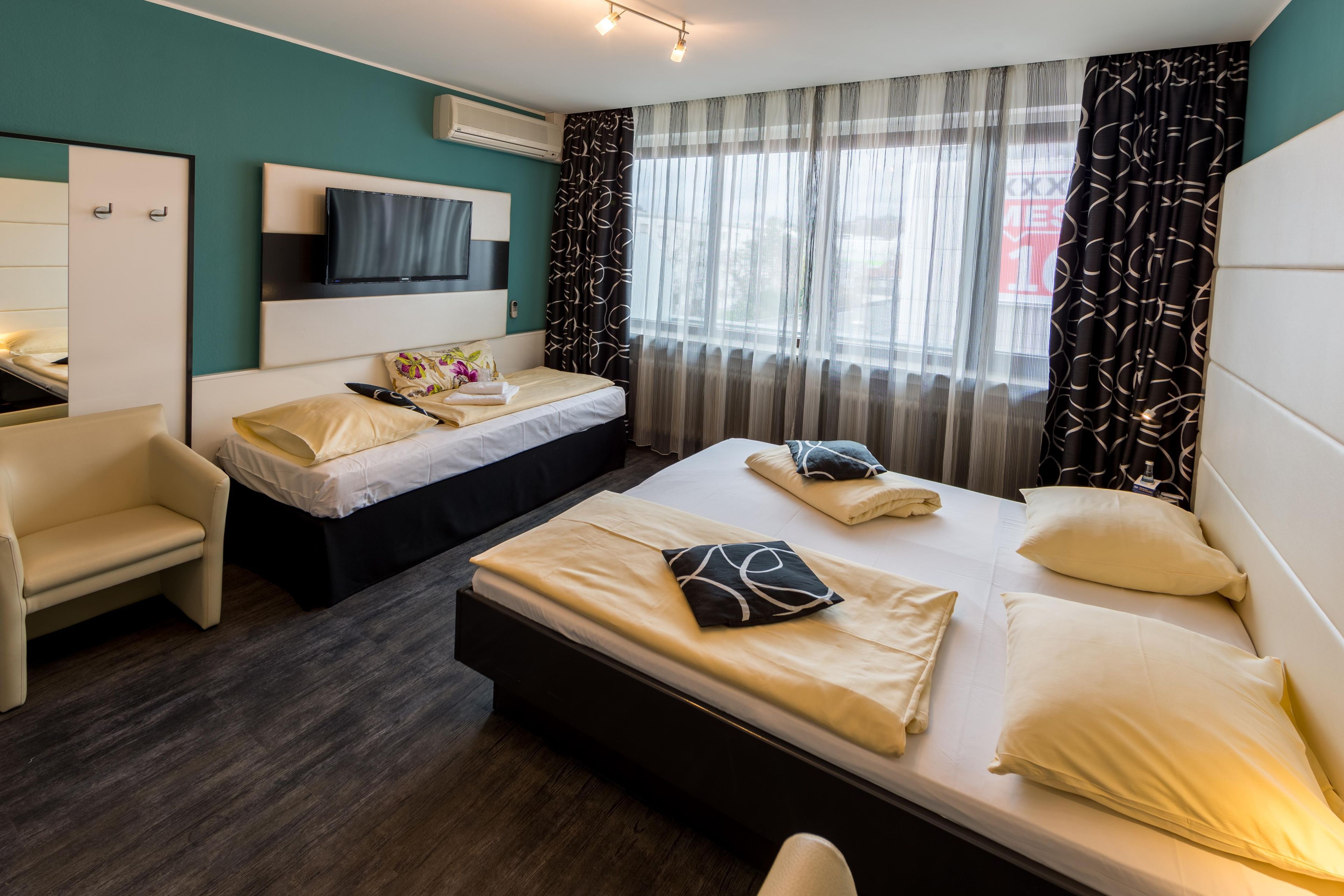 A hotel room with a bed, a chair, a TV, and a window with curtains.