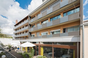 Un edificio residencial de varios pisos con balcones, mobiliario exterior y entrada de cristal.