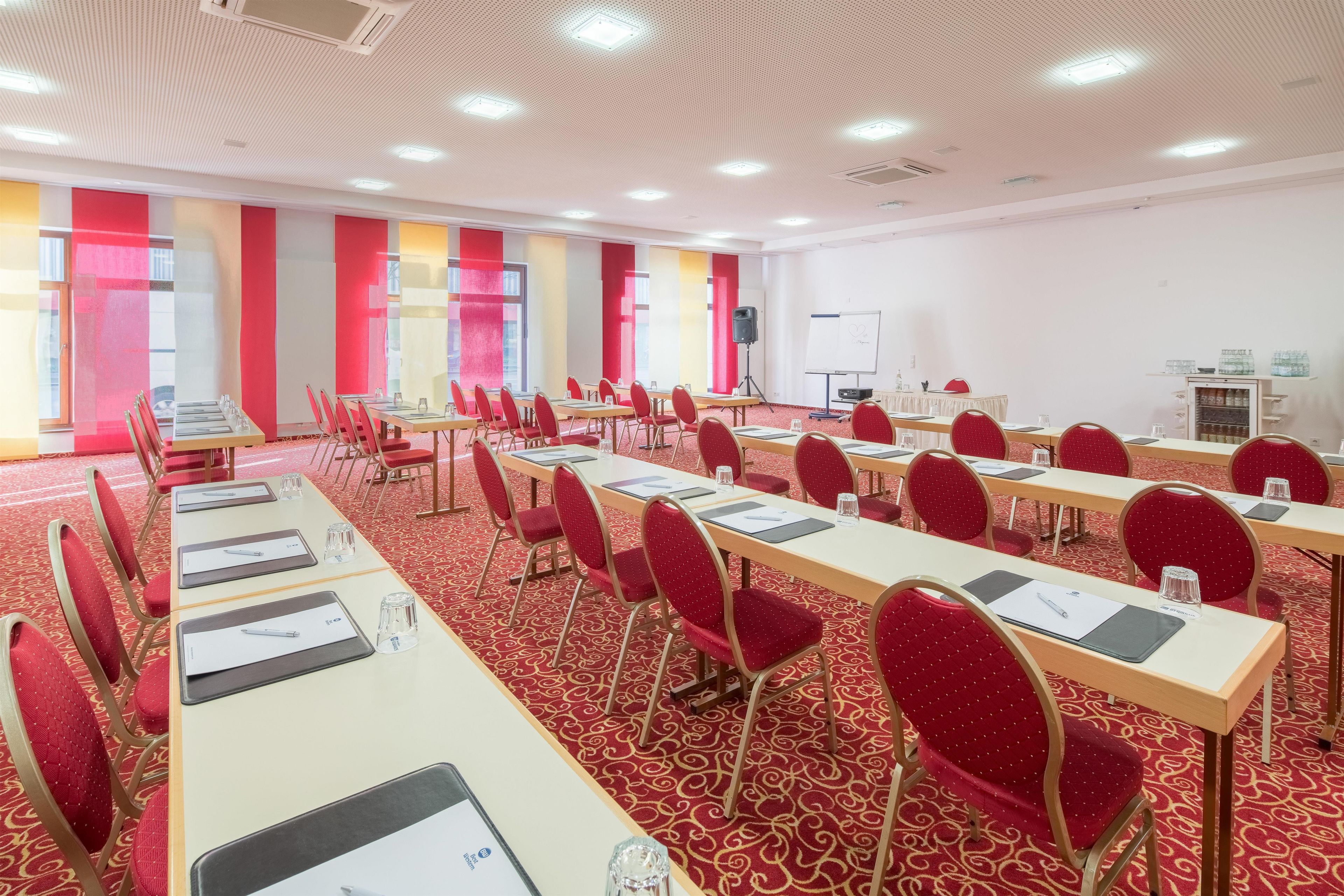A conference room with rows of tables and chairs, a whiteboard, and a projector.