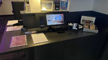 En hotellreception med en dator, en bildskärm som visar en stadsbild, en skylt som visar var parkeringen finns och en menytavla.
