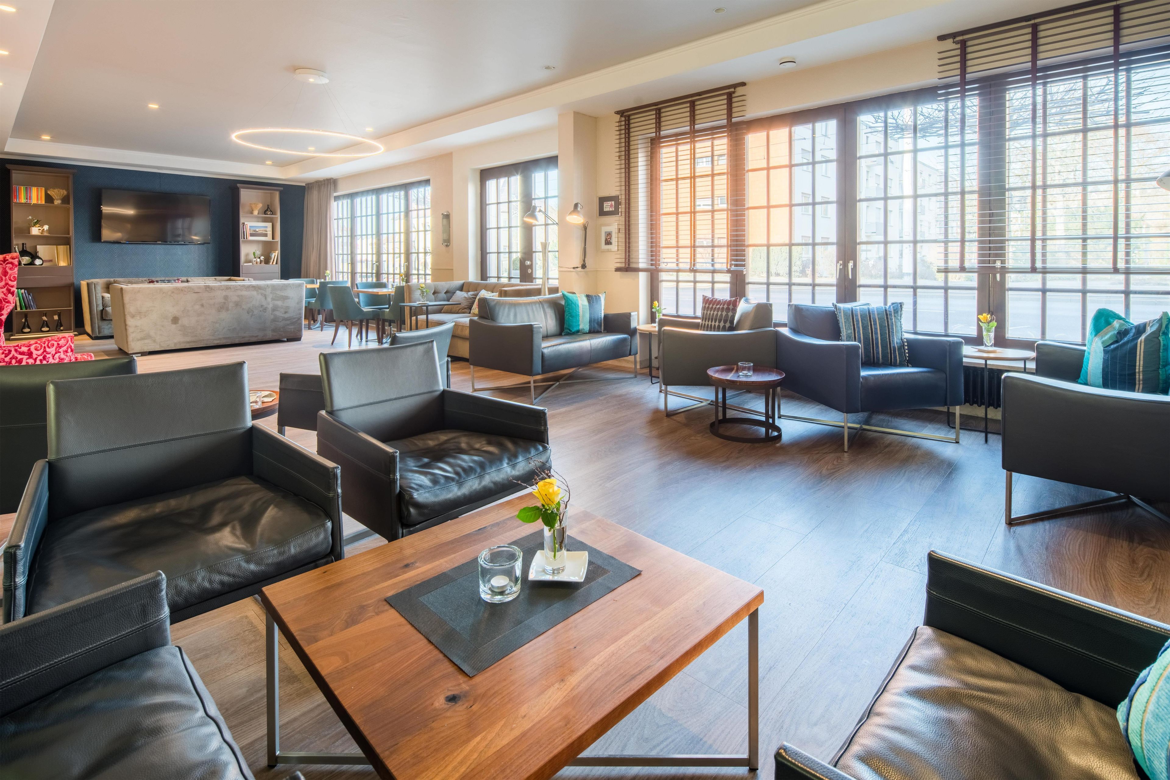 Eine geräumige Hotelhalle mit Ledersofas, einem Holztisch und großen Fenstern, die für natürliches Licht sorgen.