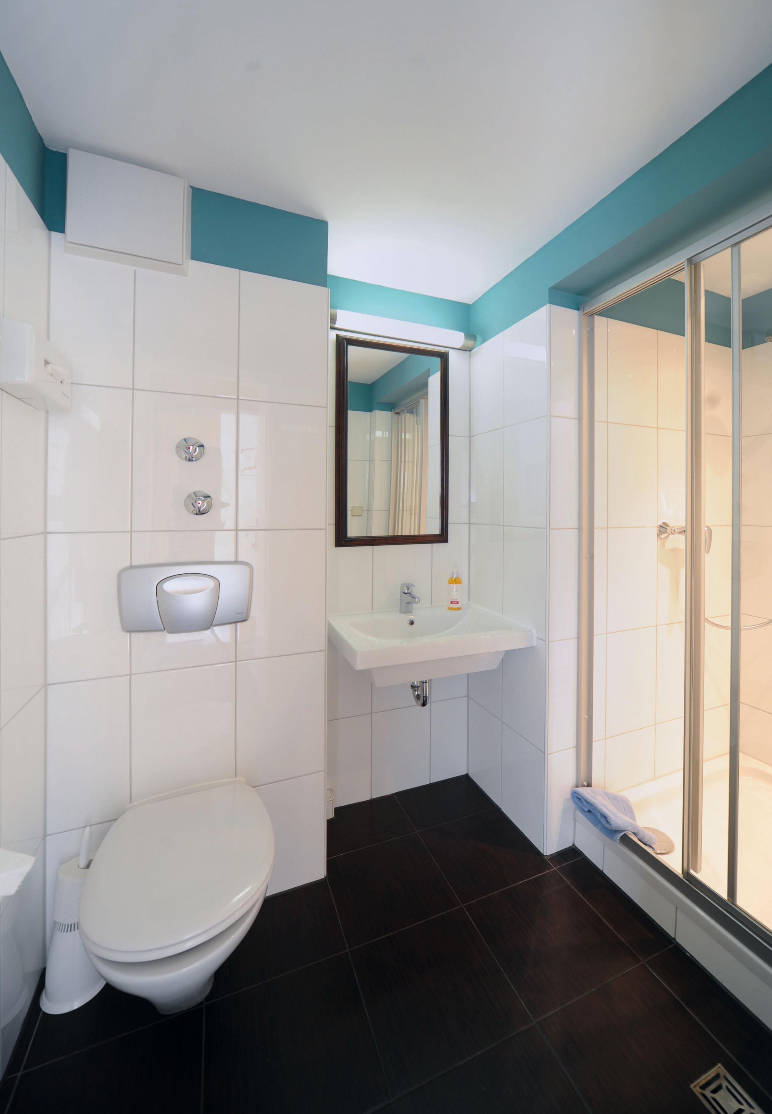 A bathroom with a toilet, sink, mirror, and a shower area.