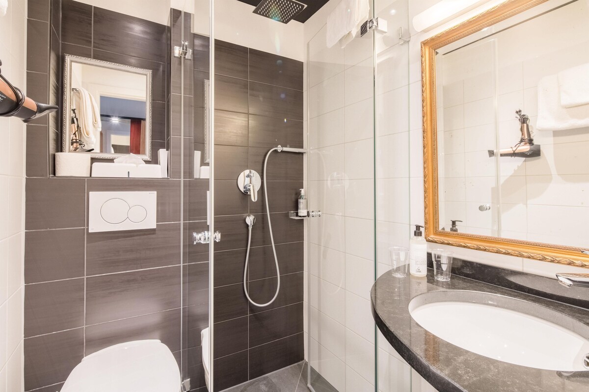 Un baño moderno con cabina de ducha de vidrio, un espejo grande con marco decorativo y encimera de mármol.