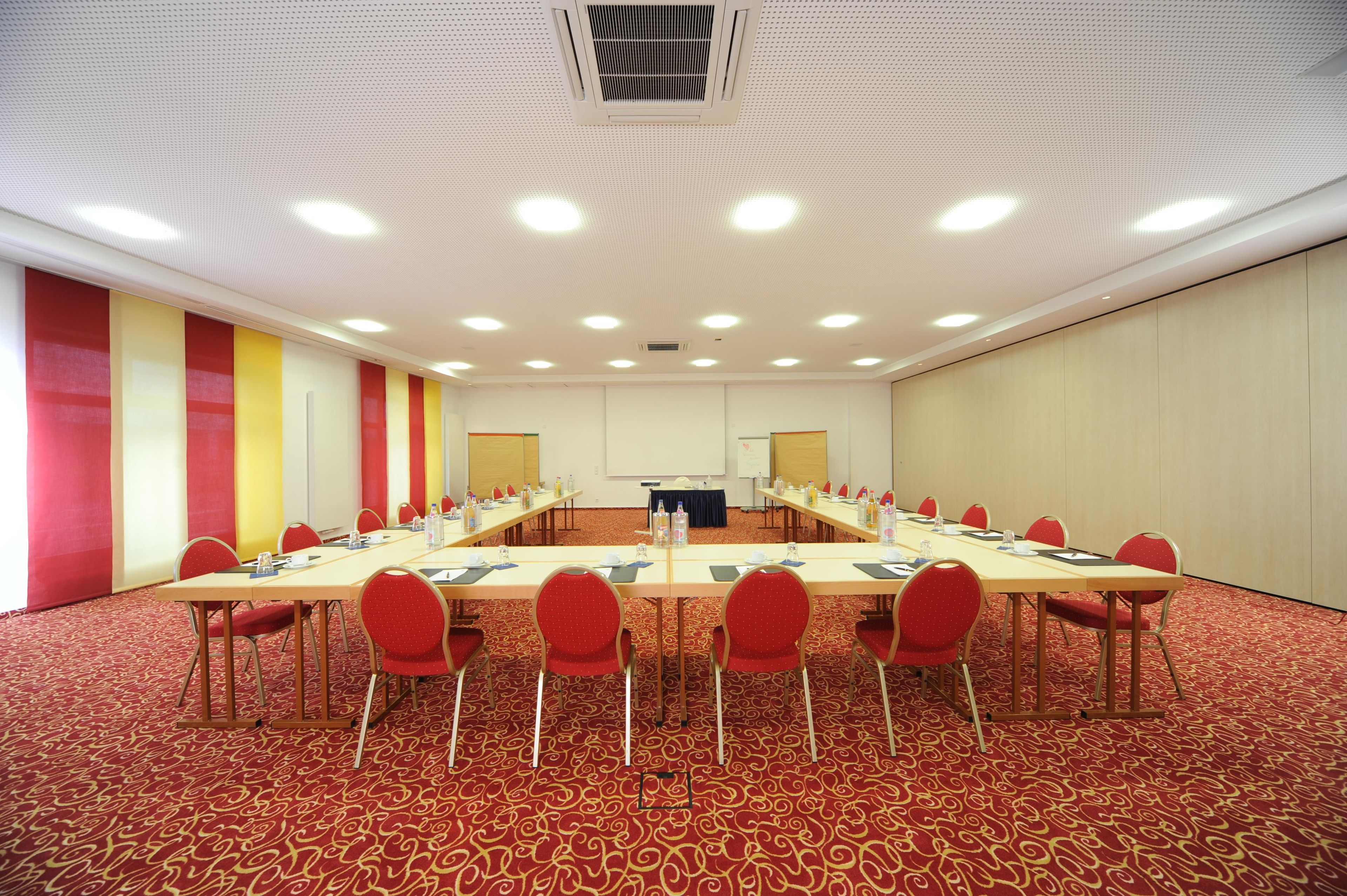 A conference room with a long table, red chairs, and a carpeted floor.