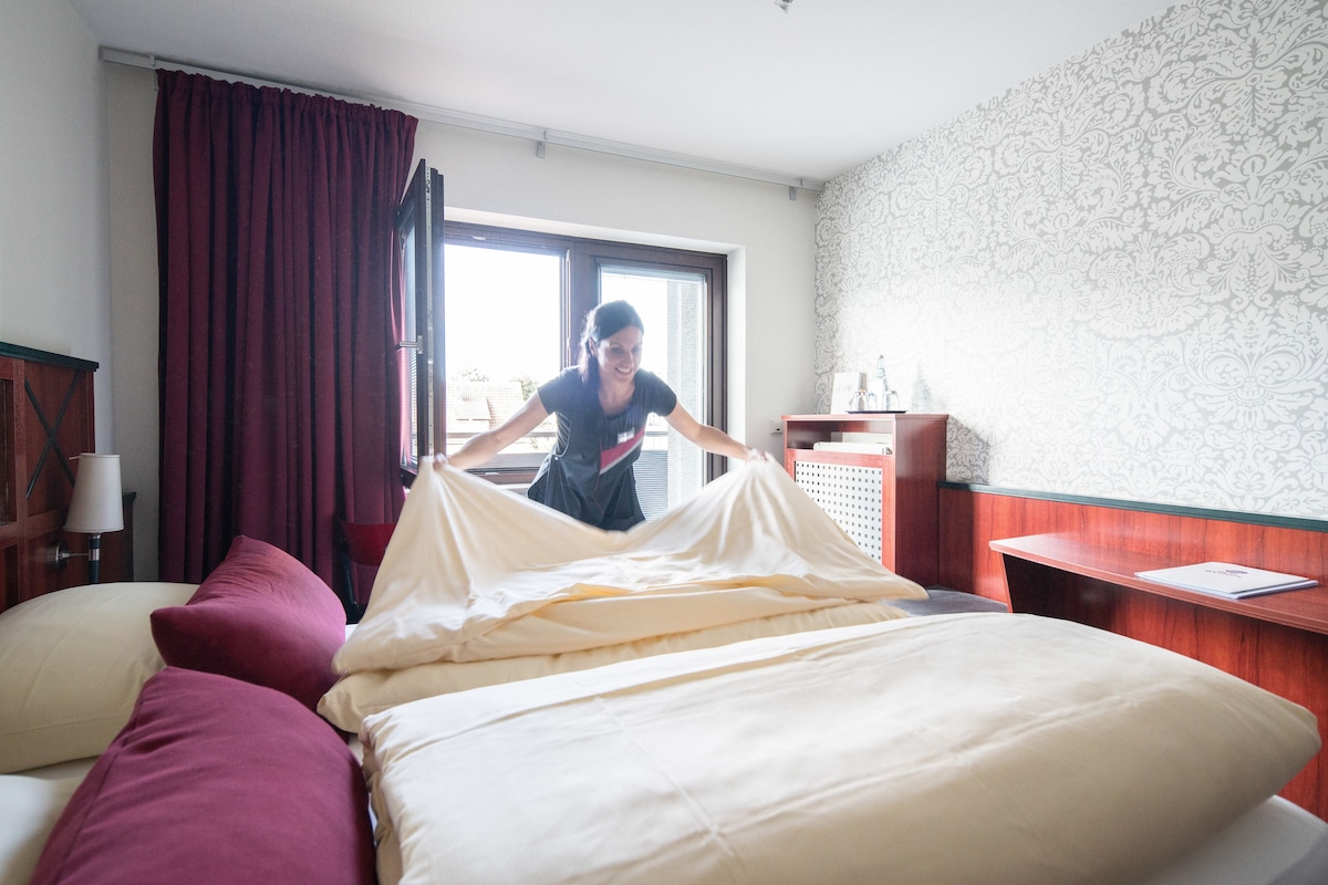 Een hotelkamer met een bed, kussens, een bureau en een raam met gordijnen.