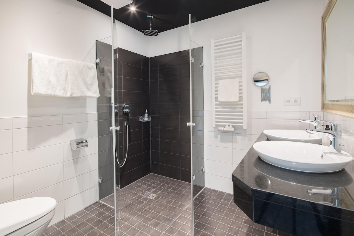 A modern bathroom with a glass-enclosed shower, two sinks, and a toilet.