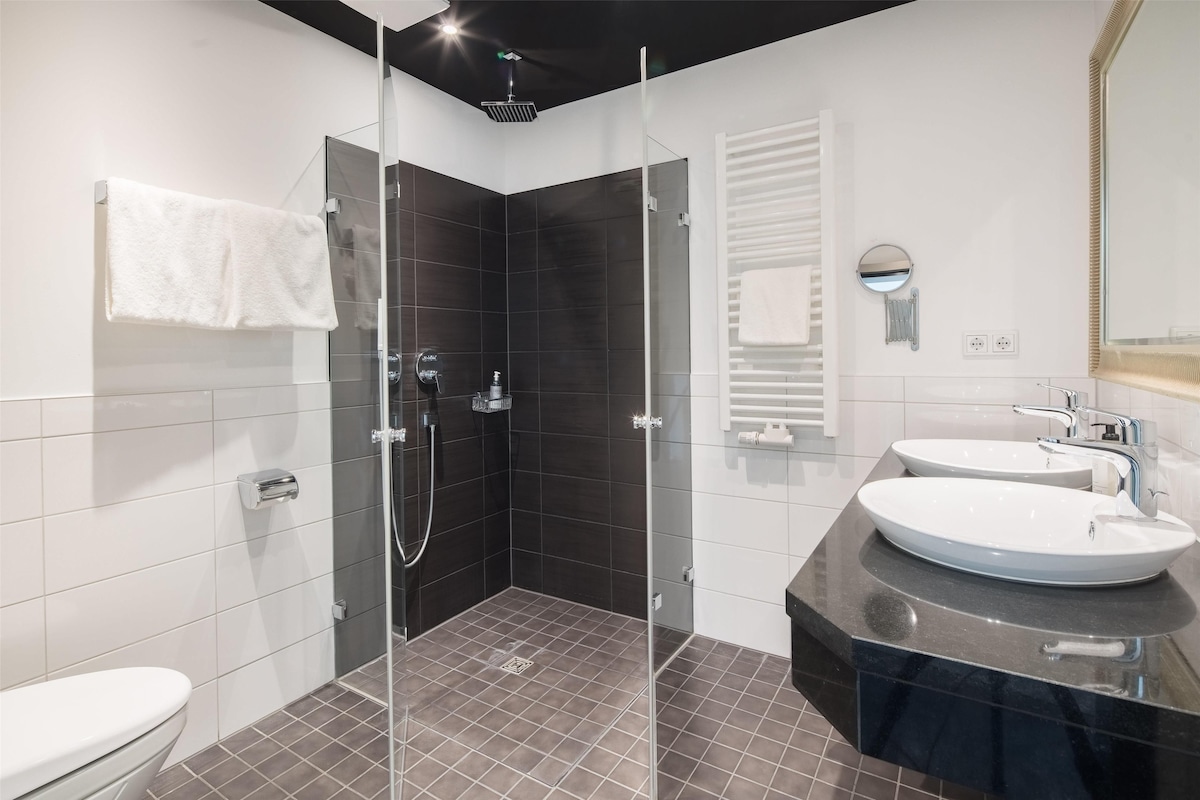 Ein modernes Badezimmer mit einer Duschkabine, zwei Waschbecken und einer Toilette.