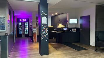 En hotellobby med en receptionsdisk, en incheckningsautomat och en bardel.