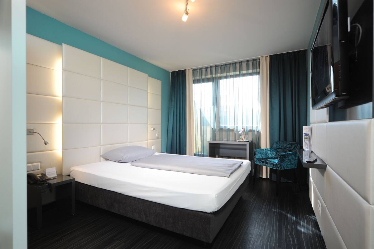 Ein Hotelzimmer mit Bett, Nachttisch, Lampe, Fernseher und Schreibtisch mit Stuhl.