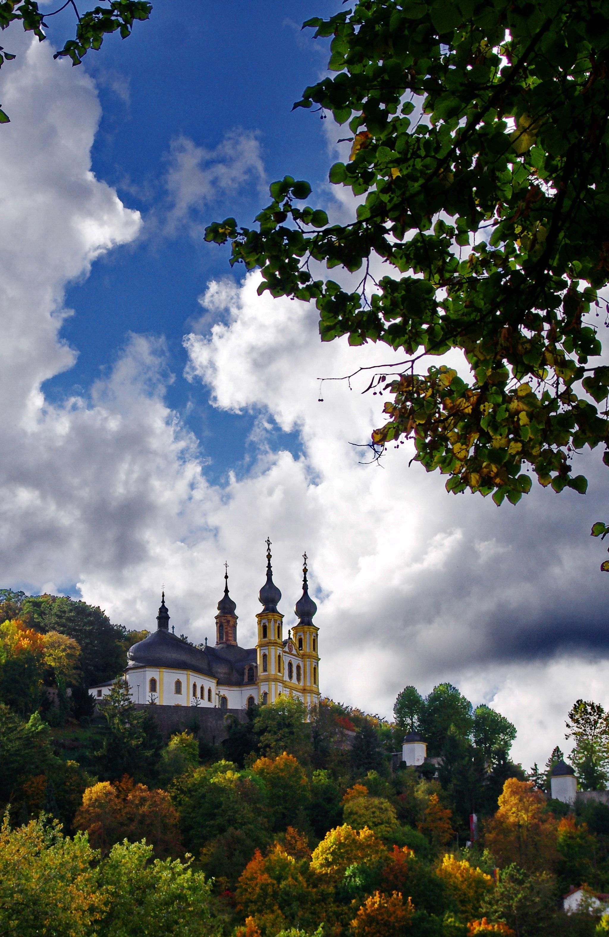 A historic building with multiple domes, surrounded by lush greenery and autumn foliage.