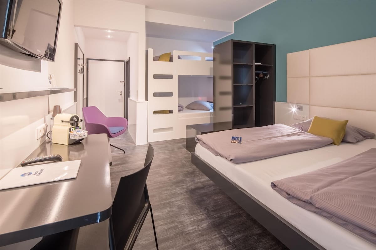 Ein modernes Hotelzimmer mit einem Bett, einem Schreibtisch mit Stuhl, einem Fernseher und einem Kleiderschrank.