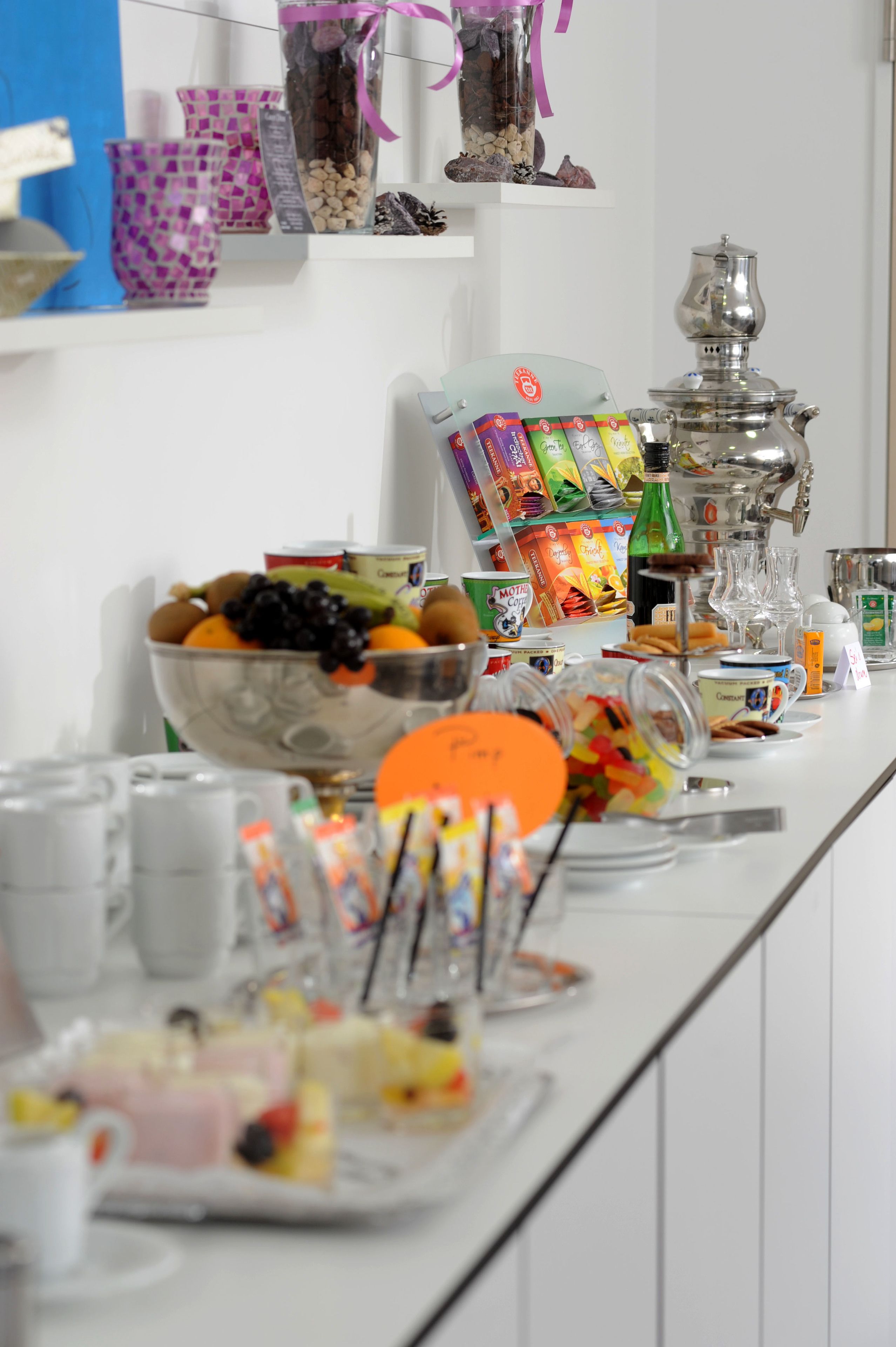 Una mesa de buffet con diversos alimentos, como un tazón de frutas, snacks empaquetados y una máquina de café.