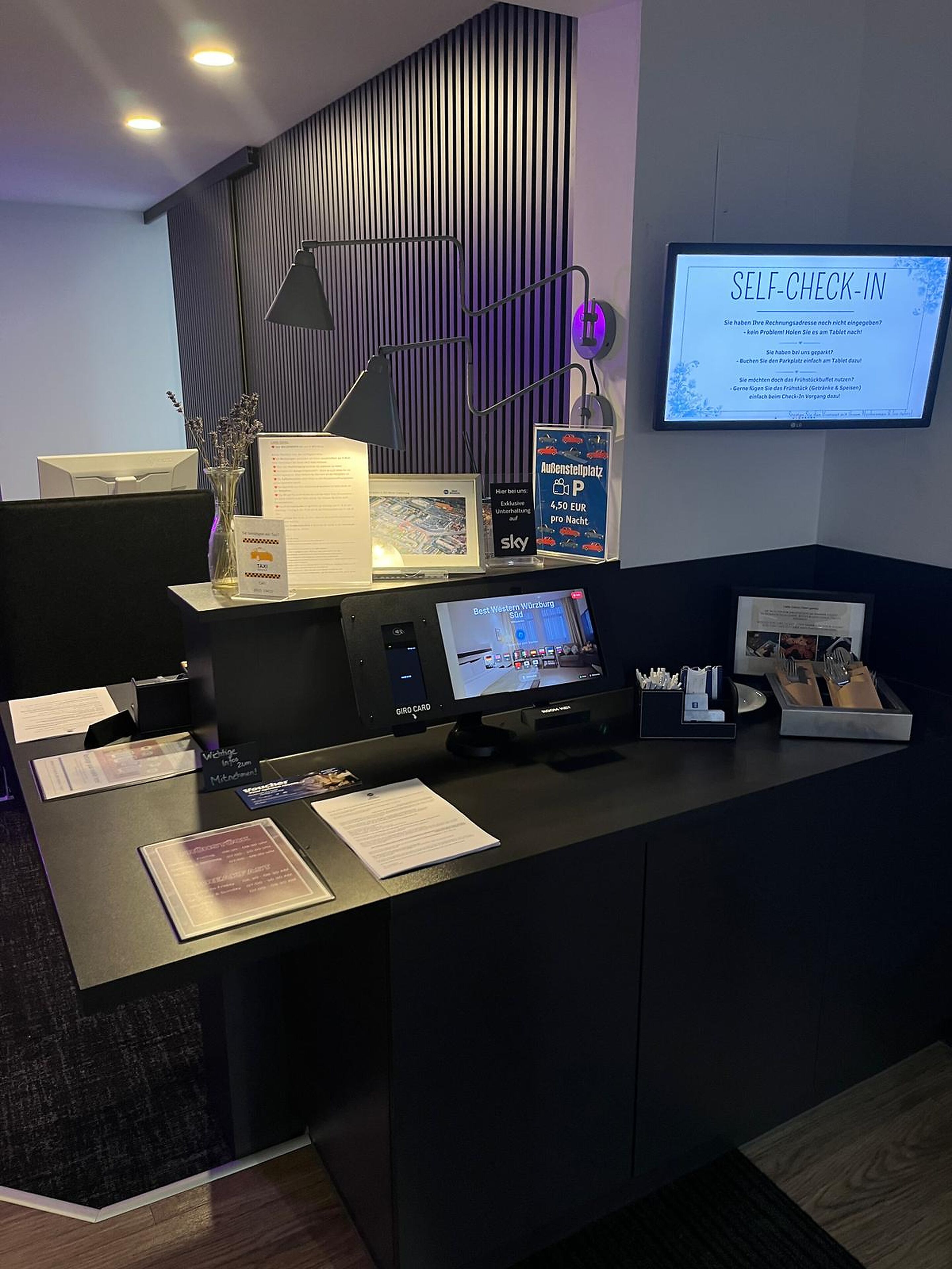 Ein Empfangsschalter mit Computer, einem Self-Check-in-Terminal und Informationsplakaten.