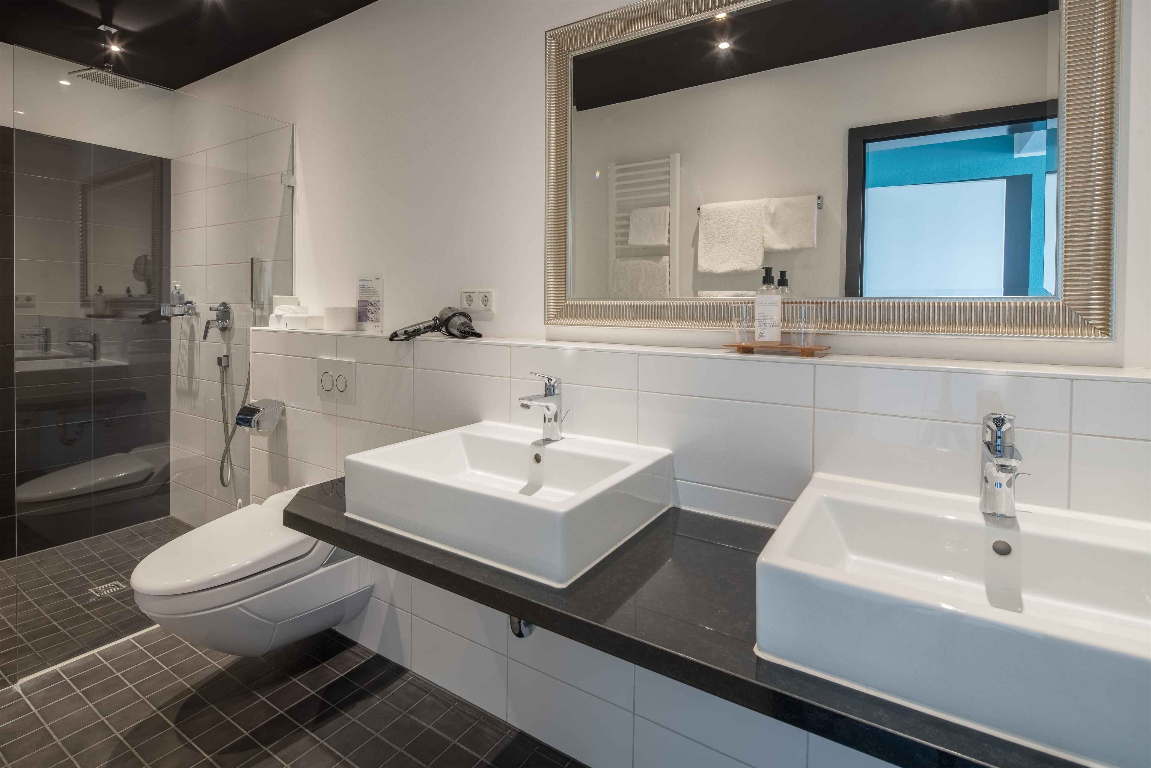 Ein modernes Badezimmer mit Dusche, zwei Waschbecken, Toilette und einem großen Spiegel.