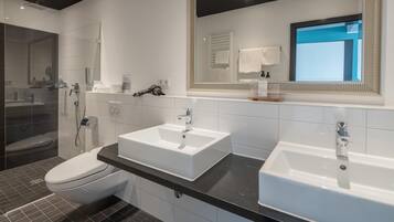 Ein modernes Badezimmer mit Dusche, zwei Waschbecken, Toilette und einem großen Spiegel.