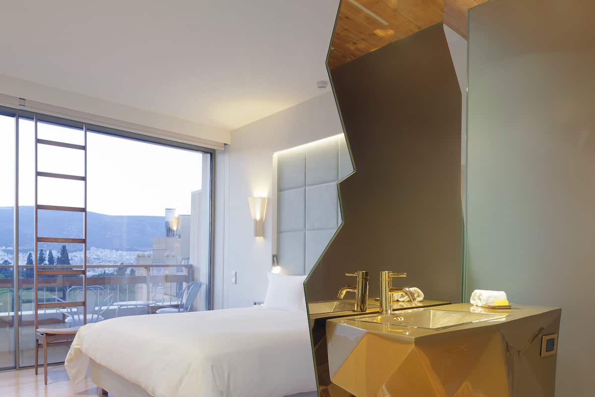 Una habitación de hotel moderna con una cama grande, un separador de vidrio y un diseño de lavamanos geométrico único.