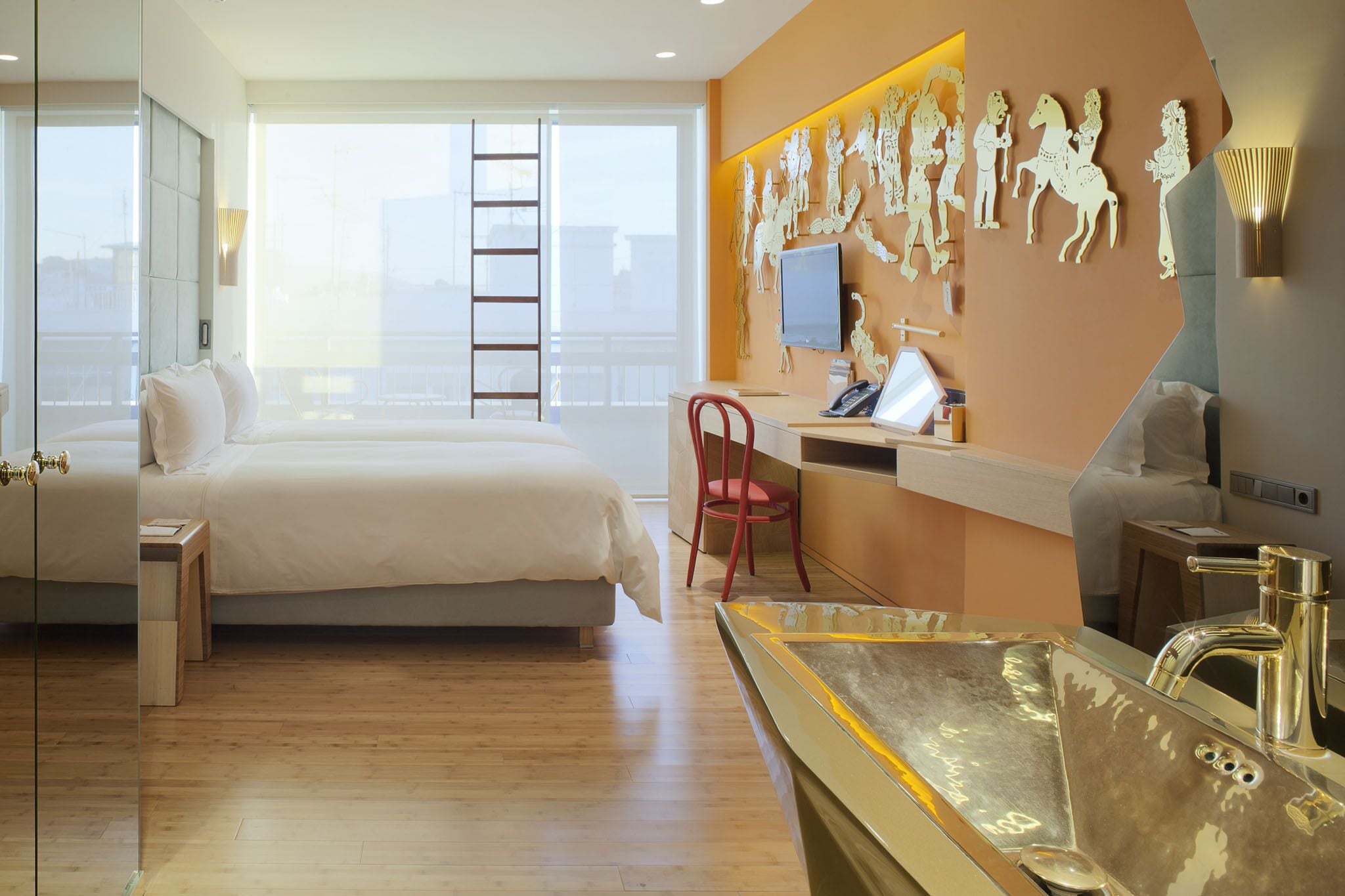 Camera d'albergo con un letto grande, una scrivania, una poltrona rossa, un'ampia finestra e un televisore montato a parete.