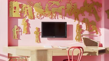 A room with a pink wall, a TV mounted on the wall, a wooden desk, and a red chair.