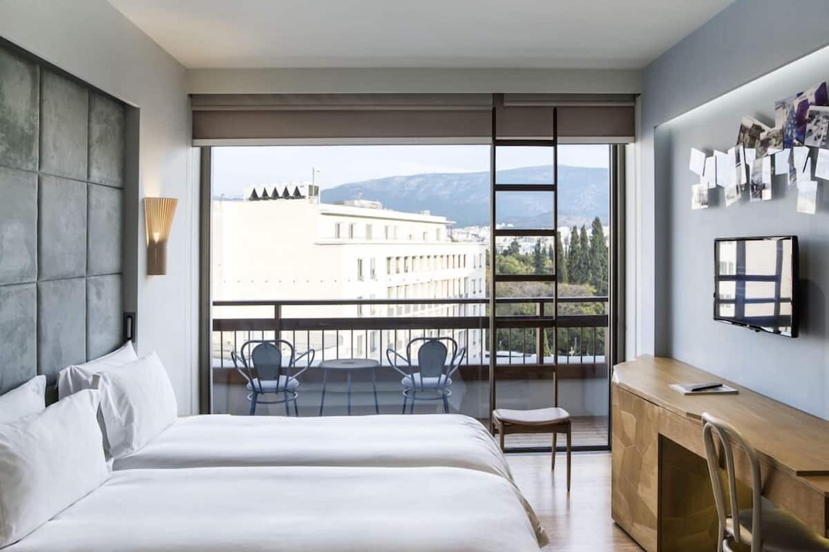Una habitación de hotel moderna con una cama grande, un escritorio y un balcón con vistas a la ciudad.