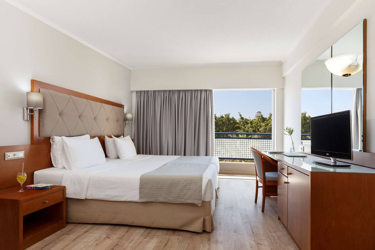 A hotel room with a bed, bedside table, TV, and a balcony with a view.