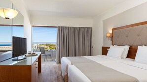 Habitación de hotel con cama, escritorio con televisor, silla y vista al mar.