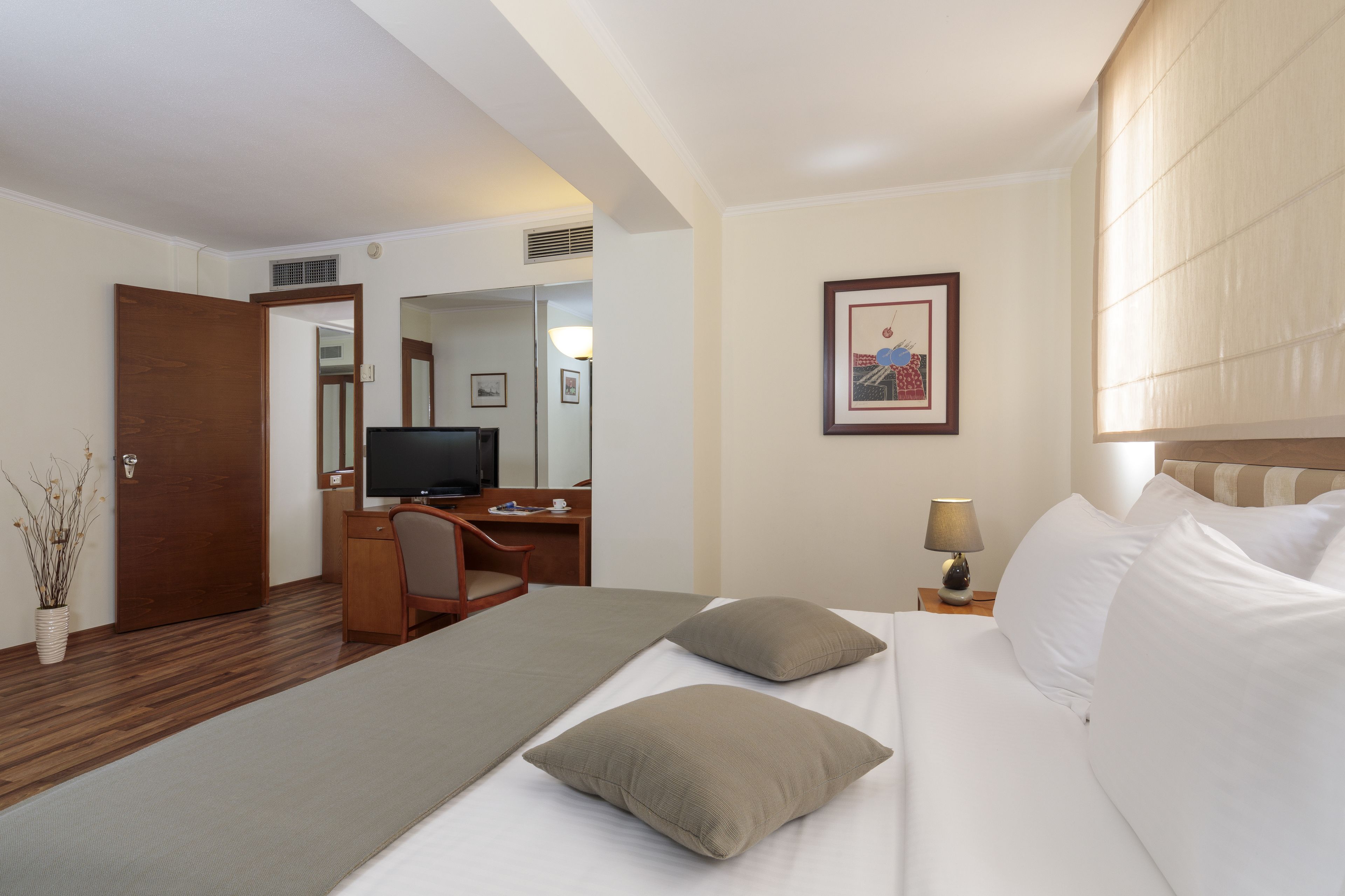 Habitación de hotel con cama, escritorio, televisión y lámpara.