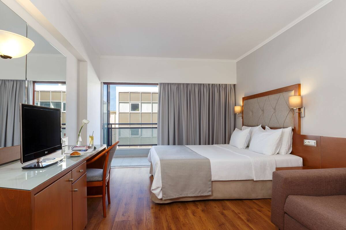 A hotel room with a bed, a desk with a TV, a chair, and a couch.