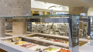 Zona de bufé con diversas opciones de comida, como carnes, quesos y verduras, en un ambiente interior bien iluminado.