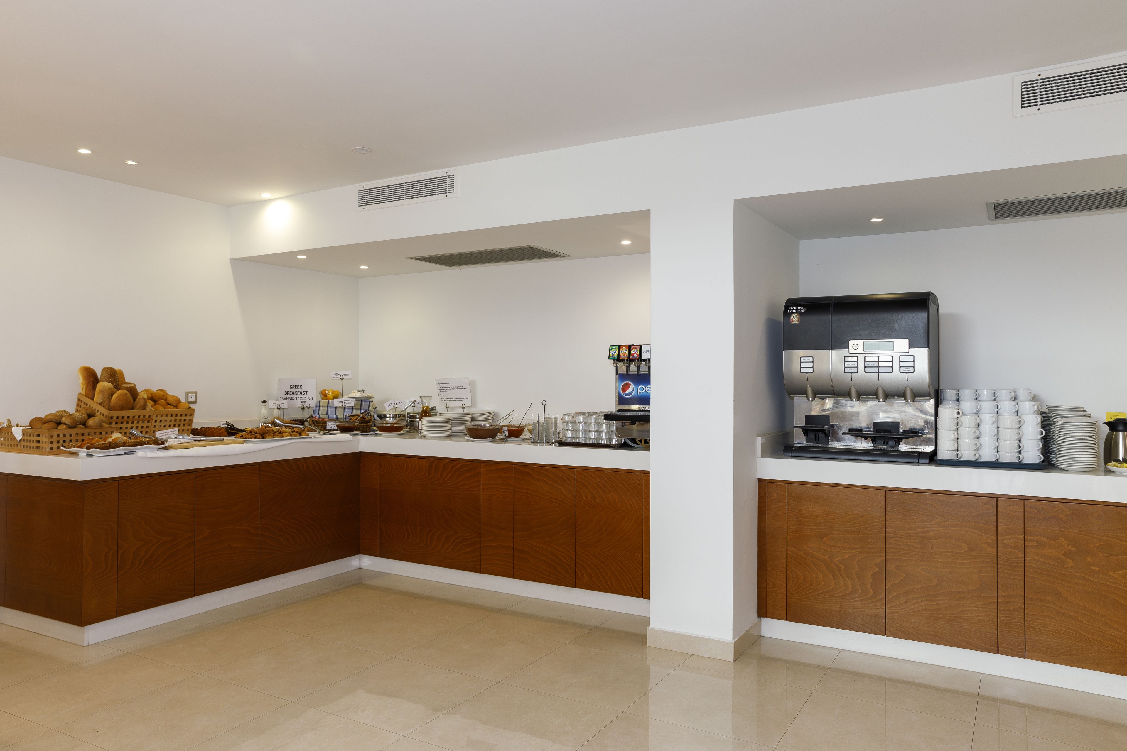 A modern breakfast bar with a wooden finish, equipped with a coffee machine, a water dispenser, and a variety of breakfast items.