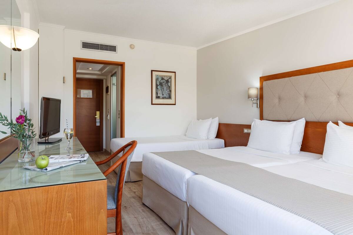 A hotel room with a bed, a desk with a computer, a chair, and a small table with a glass top.