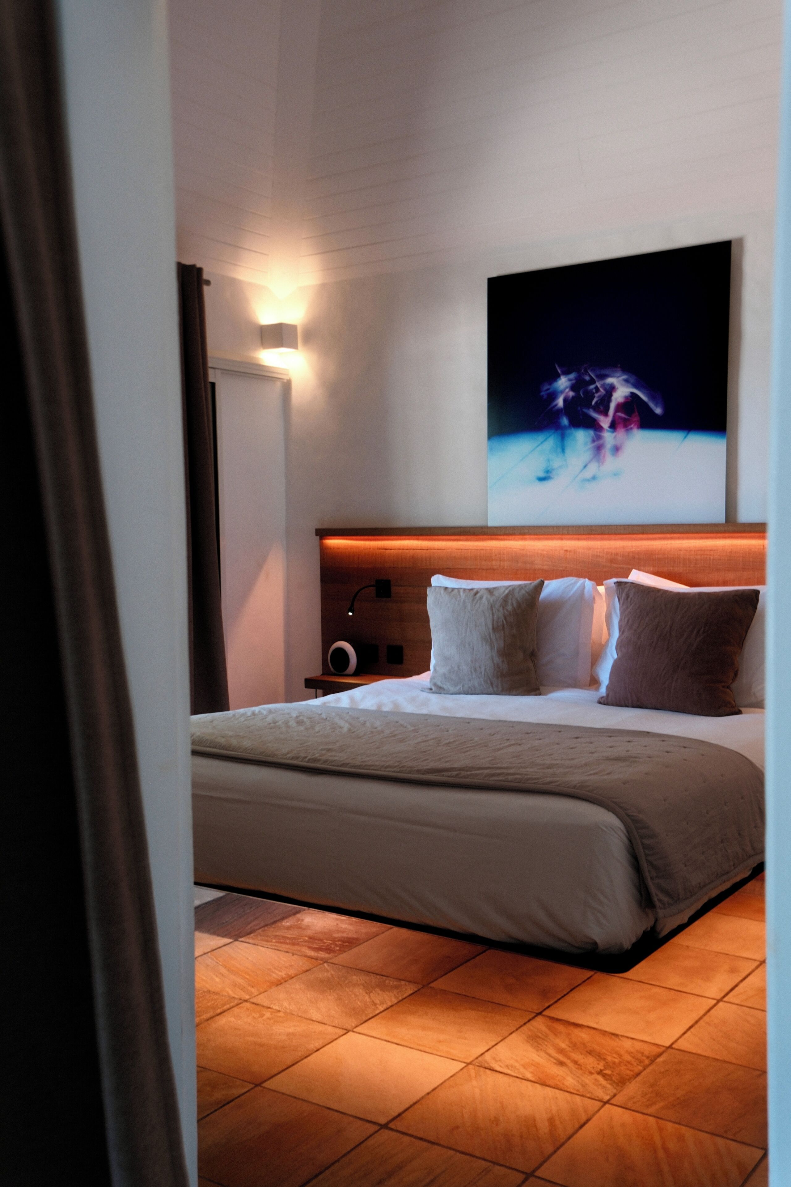 Une chambre d’hôtel avec un lit, une table de chevet, une lampe fixée au mur et un tableau.