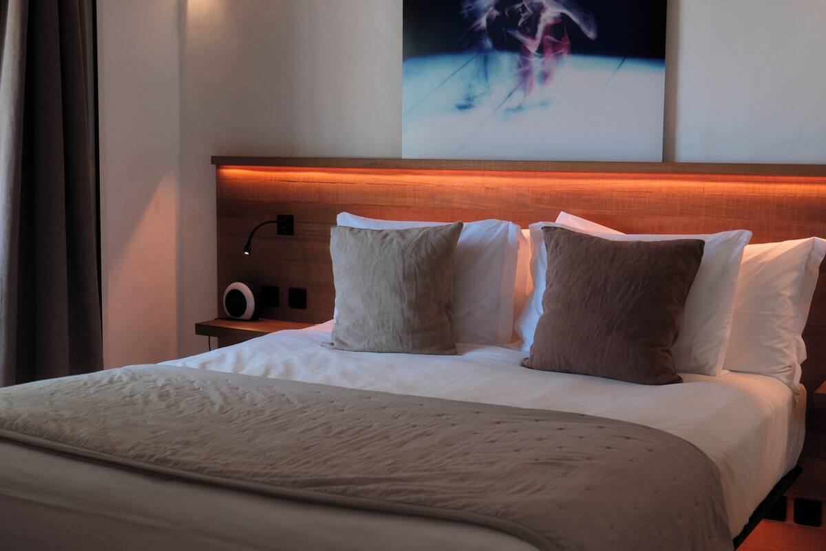 A hotel room with a large bed, a nightstand with a lamp, and a painting on the wall.