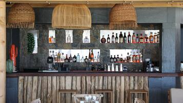 Una zona de bar con mostrador de madera, estantes llenos de botellas de licor y lámparas colgantes de fibras naturales.