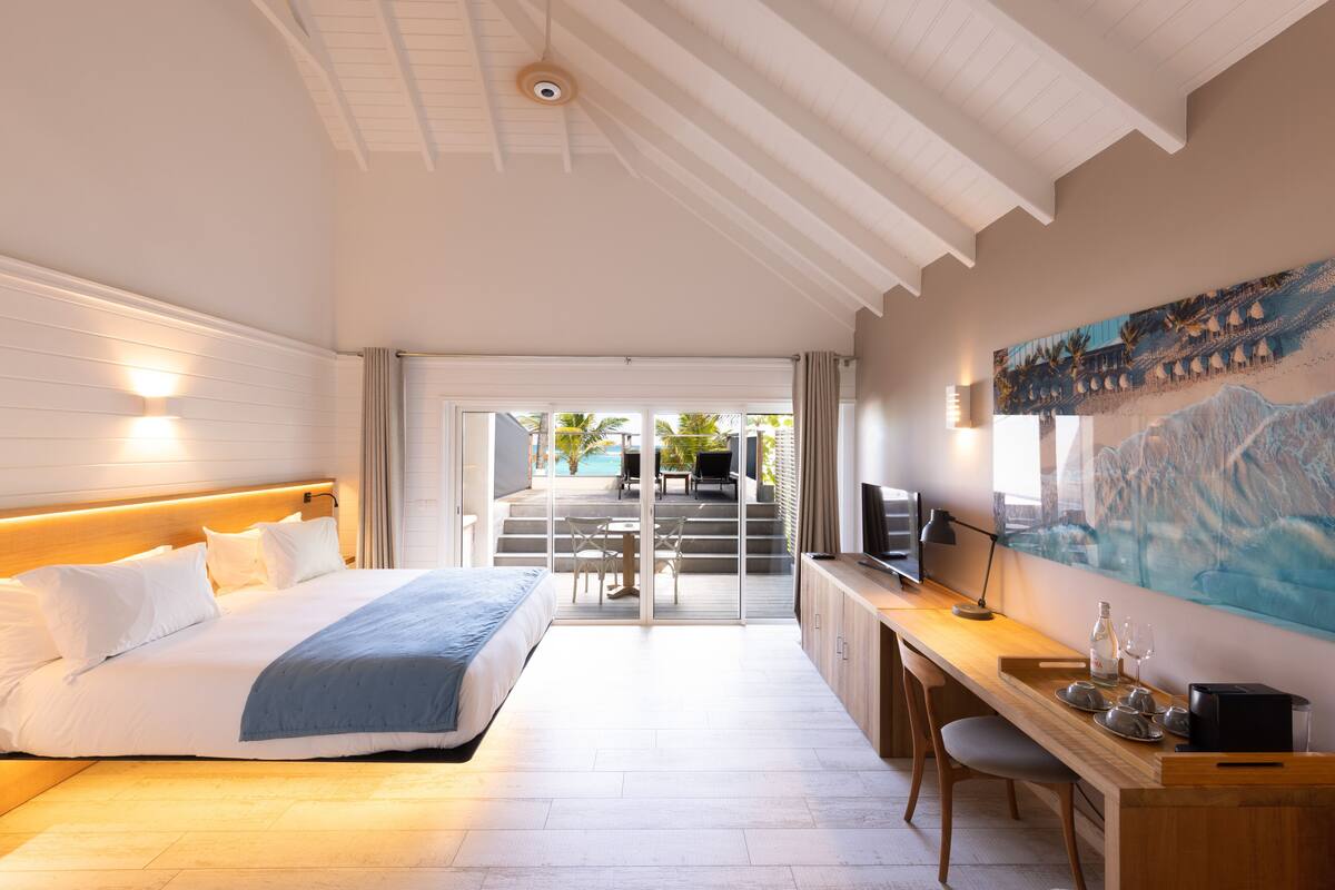 A modern hotel room with a large bed, a desk, and a view of the pool area.