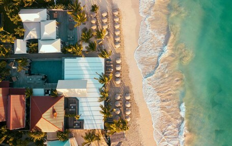 An aerial view of a beachfront resort with a swimming pool, beach umbrellas, and palm trees.