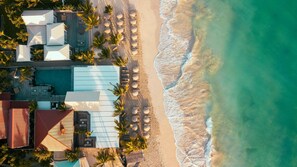 Vista aérea de un resort frente a la playa, con piscina, sombrillas y palmeras.
