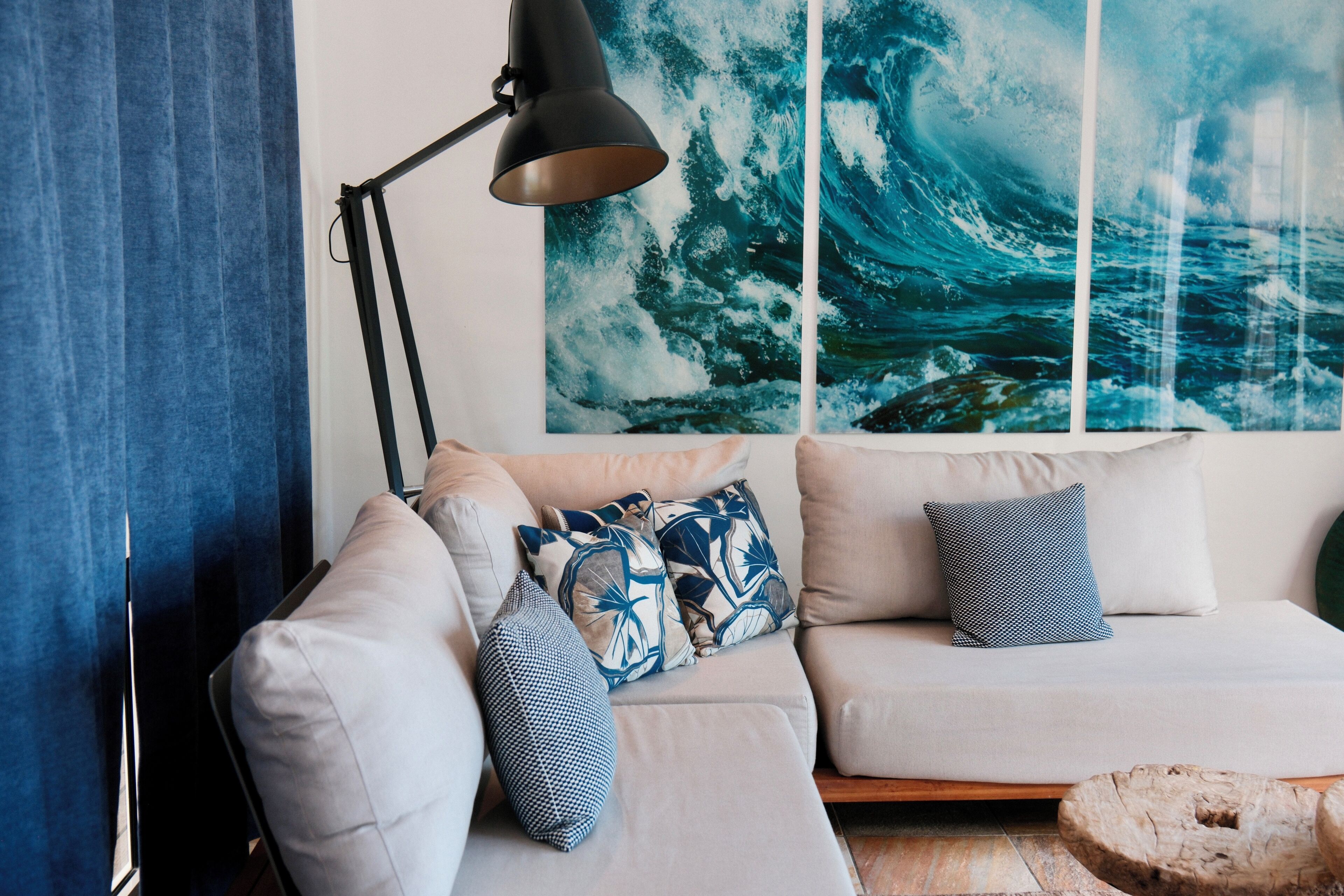 A modern living room with a sofa, decorative pillows, a floor lamp, and a large ocean wave painting on the wall.