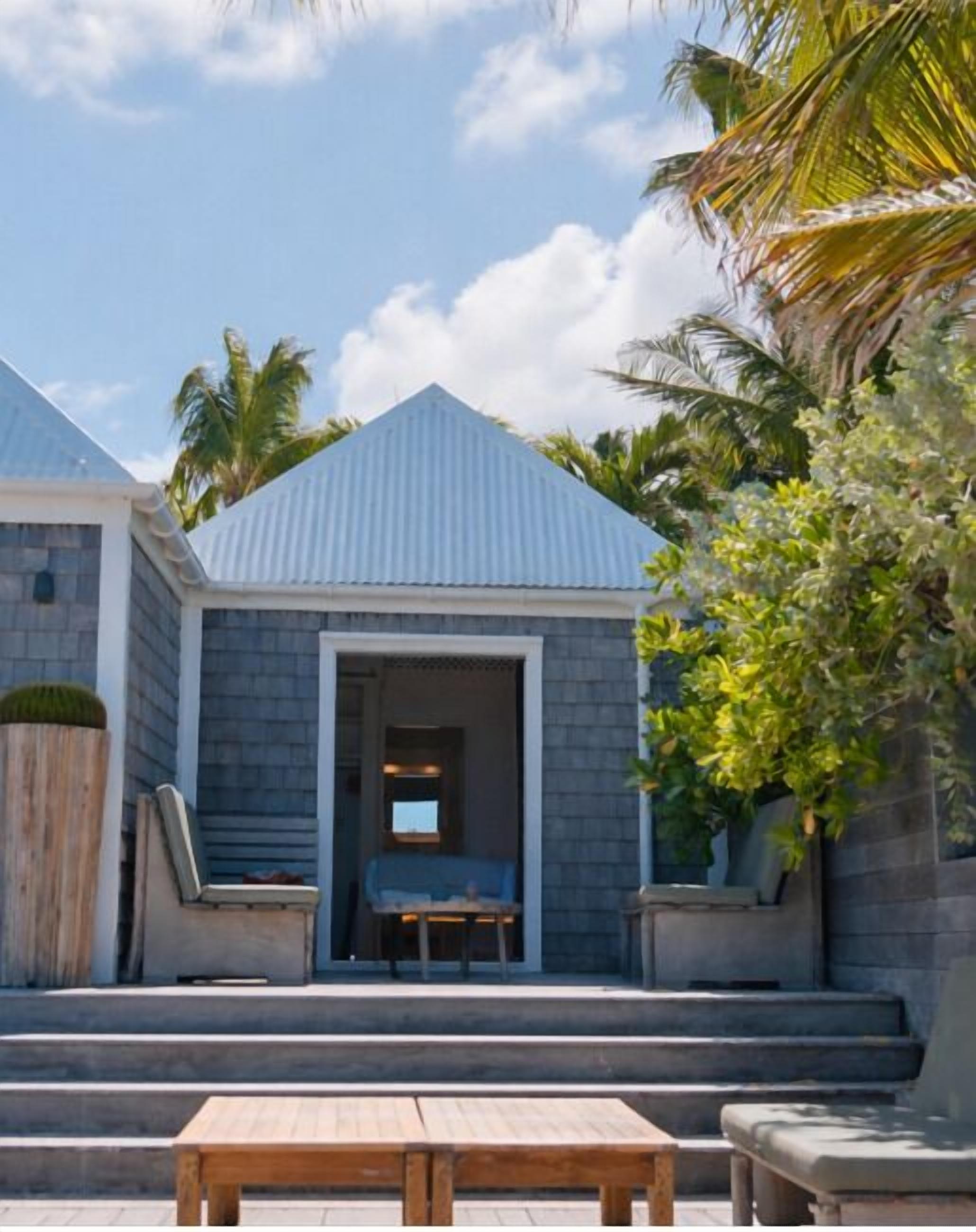 A building with a sloped roof, a covered entrance, and a wooden table in the foreground.