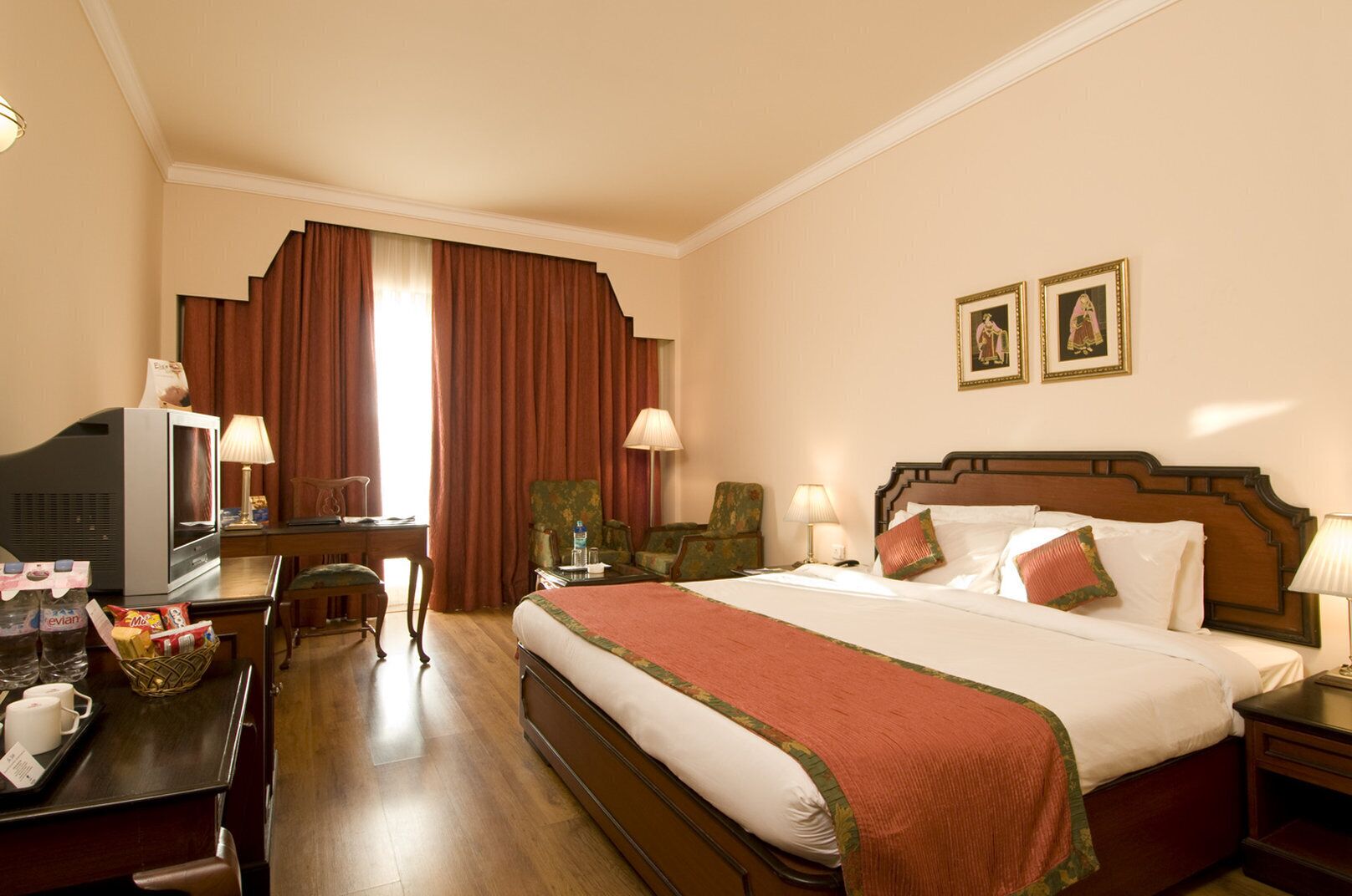 Una habitación de hotel con cama, escritorio con televisor, silla, mesita de noche y lámpara.