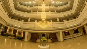 Un hall d’hôtel à plusieurs niveaux, doté d’un lustre central, d’espaces aménagés pour s’asseoir et d’un comptoir d’accueil.