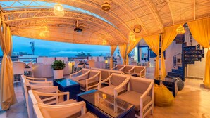 Un salon sur le toit, doté d’un espace extérieur avec des sièges, d’une table en verre et offrant une vue sur le paysage urbain.