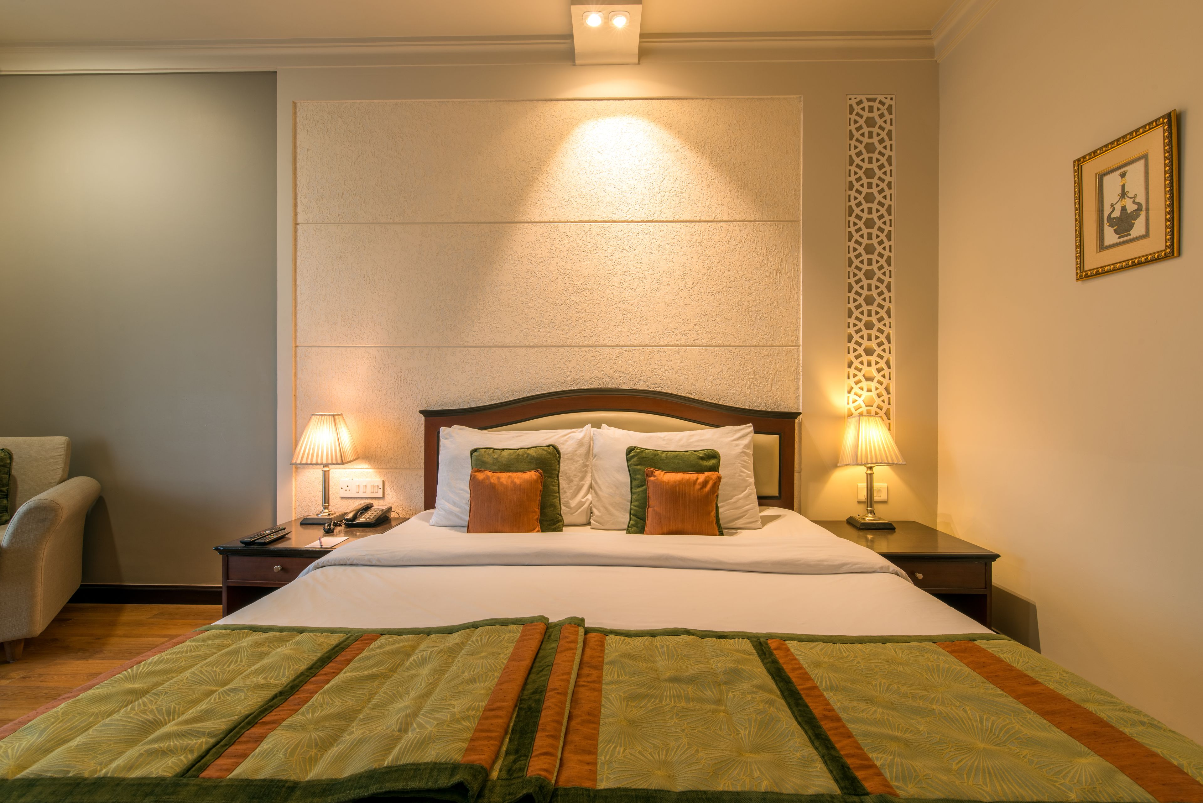 Une chambre d’hôtel avec un grand lit, deux lampes de chevet, une chaise et un panneau décoratif au mur.