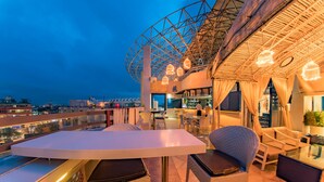 Un espace extérieur aménagé avec des meubles en osier, un bar et une vue sur le paysage urbain.