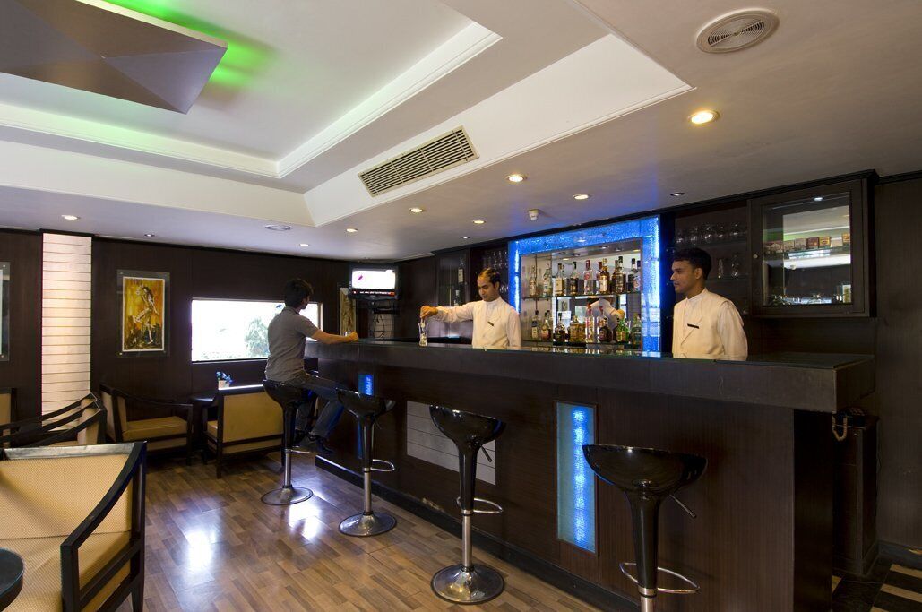 A bar area with a counter, stools, and a bartender. There are chairs and tables in the foreground.