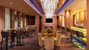 A modern bar area with round tables and bar stools, a large chandelier, and a flat-screen TV mounted on the wall. - Vivanta Ernakulam, Marine Drive (Kanayannur)