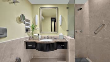 Une salle de bain moderne avec un lavabo surmonté d’un plan de travail en granit, un grand miroir, un porte-serviettes et une douche à l’italienne.