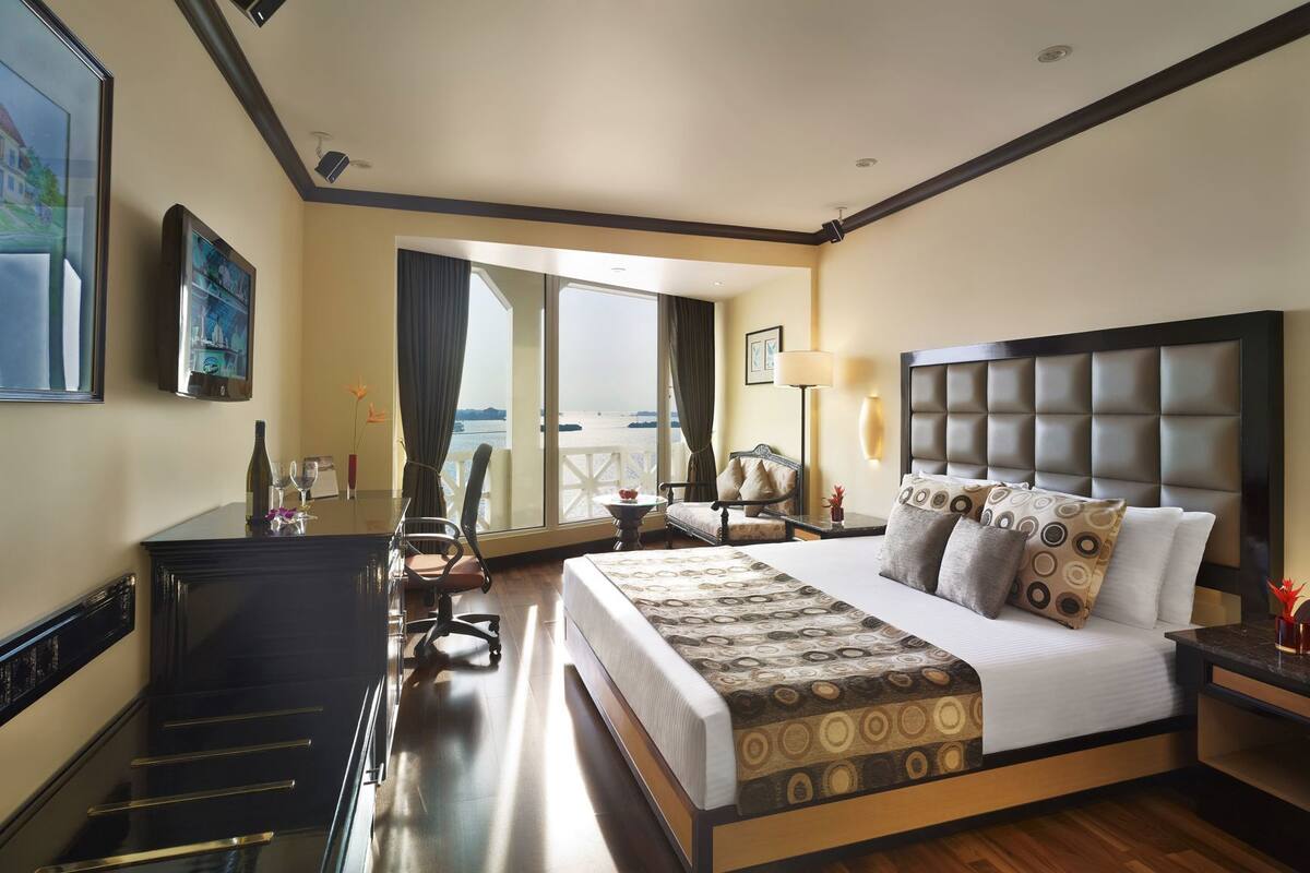 A hotel room with a large bed, a desk, a chair, a view of the sea, and a balcony.
