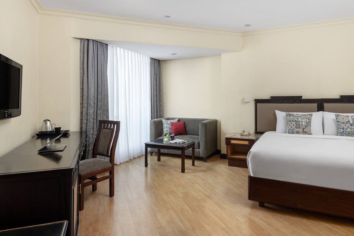 A hotel room with a bed, a desk, a chair, a coffee table, and a TV.