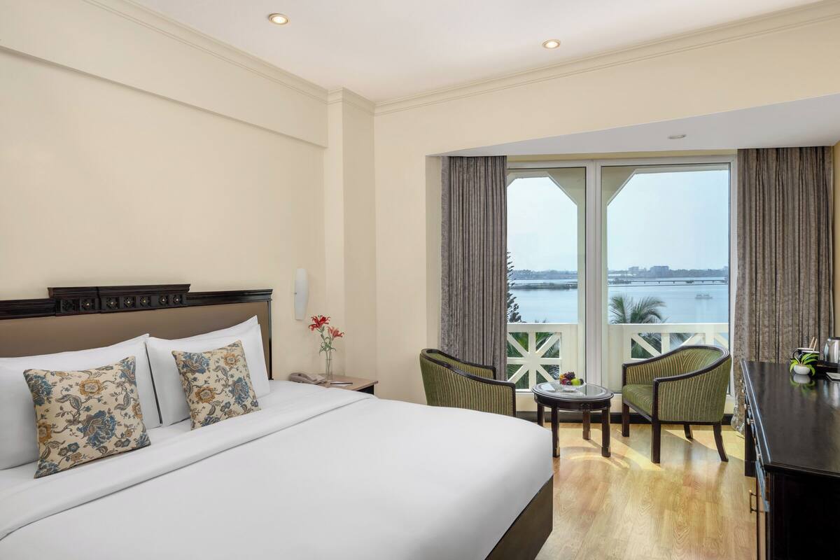 A hotel room with a large bed, two chairs, a small table, and a balcony with a view of the water.
