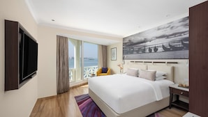 A modern hotel room with a large bed, a flat-screen TV, a balcony with a view of the sea, and a painting on the wall. - Vivanta Ernakulam, Marine Drive (Kanayannur)